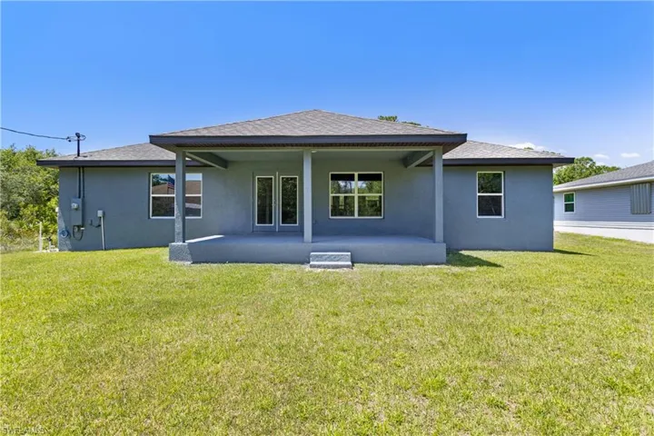 Rear view of property with a lawn, a shingled roof, a patio area, and stucco siding