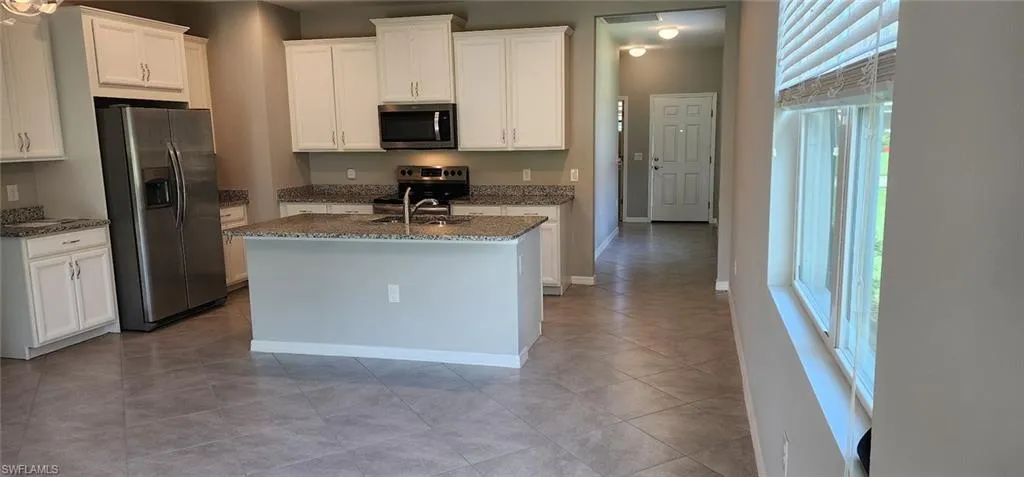 Kitchen with stainless steel appliances, a healthy amount of sunlight, an island with sink, and white cabinetry