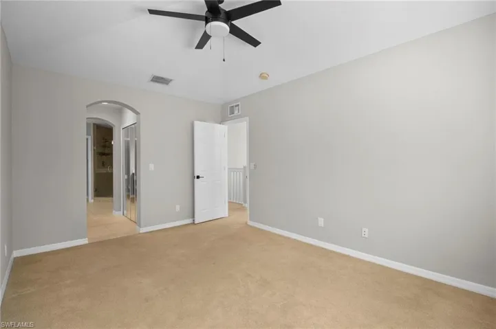 Unfurnished bedroom featuring arched walkways, a ceiling fan, light colored carpet, connected bathroom, and vaulted ceiling