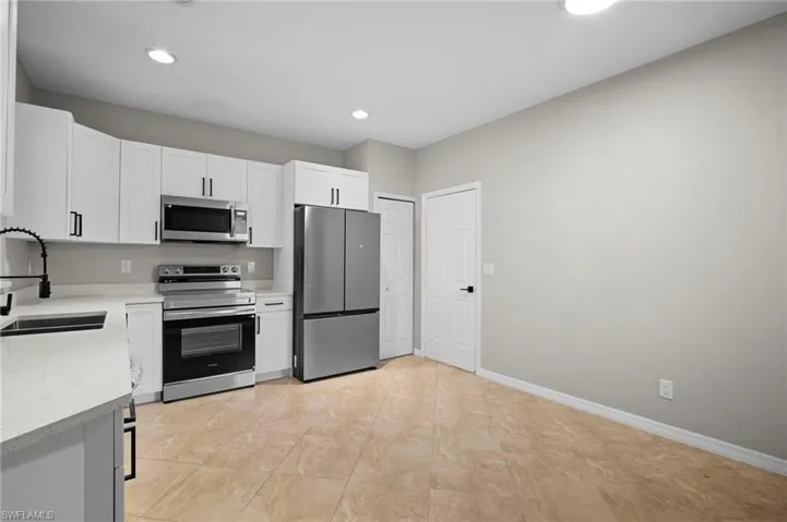 Kitchen with appliances with stainless steel finishes, white cabinetry, light stone counters, and recessed lighting