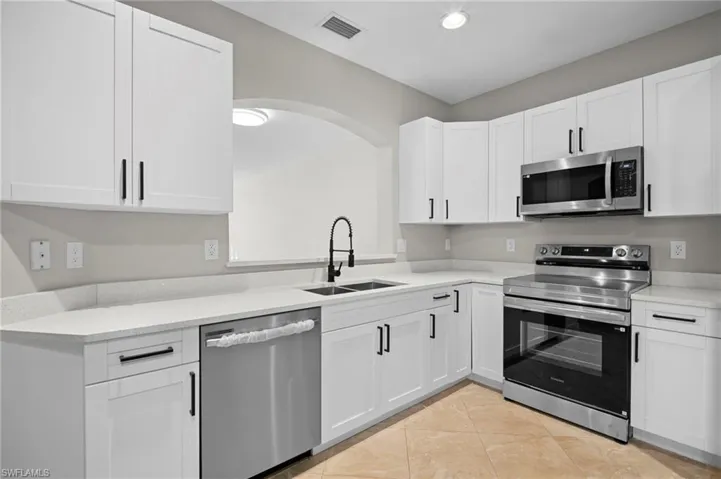 Kitchen with appliances with stainless steel finishes, white cabinets, light stone counters, light tile patterned floors, and recessed lighting