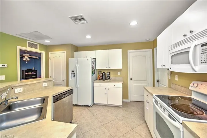 Kitchen with white appliances, white cabinets, sink, ceiling fan, and light tile patterned floors