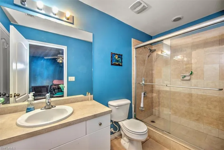Bathroom featuring ceiling fan, toilet, a shower with door, and vanity