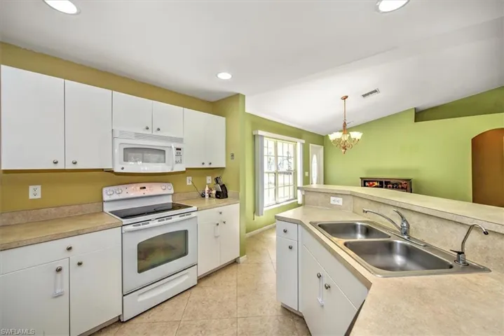 Kitchen featuring sink, white cabinets, hanging light fixtures, and white appliances
