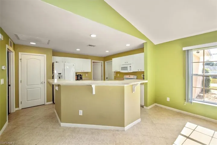 Kitchen with a breakfast bar, a center island, lofted ceiling, white appliances, and white cabinetry