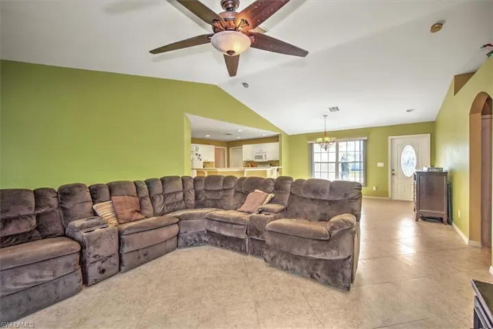 Living room featuring lofted ceiling, light tile patterned flooring, and ceiling fan with notable chandelier