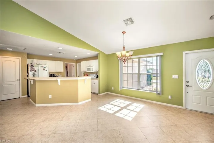 Kitchen featuring pendant lighting, white appliances, lofted ceiling, white cabinets, and a chandelier