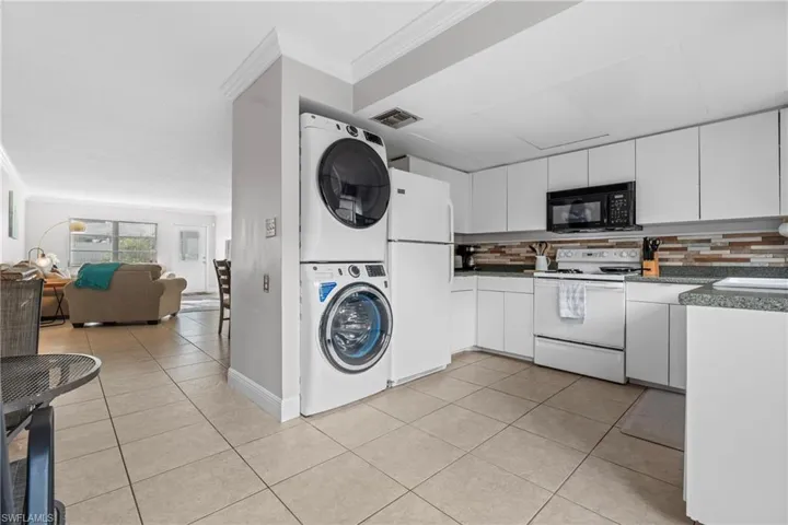 Laundry area with ornamental molding, light tile patterned floors, and stacked washer and dryer