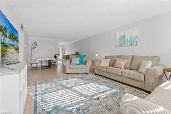 Living room with light tile patterned floors, ornamental molding, and a textured ceiling