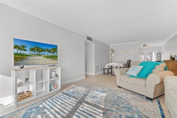 Living room with light tile patterned flooring, ornamental molding, a textured ceiling, and ceiling fan