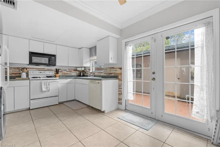 Kitchen with white appliances, ornamental molding, white cabinetry, light tile patterned flooring, and french doors