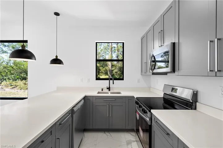 Modern kitchen featuring light gray cabinetry, white countertops, stainless steel appliances, and black pendant lighting