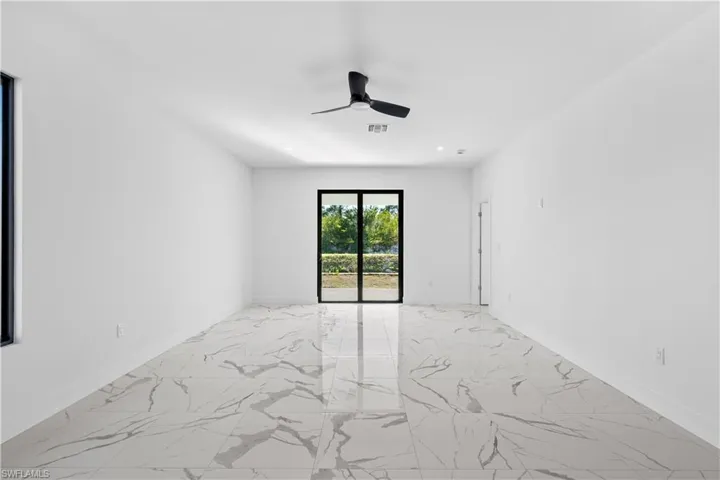 Spacious room featuring large format marble-look tile flooring, white walls, and a modern black ceiling fan