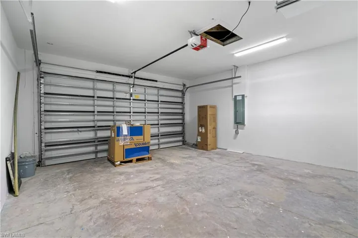 Spacious garage featuring a concrete floor, bright overhead lighting, a sectional garage door, and a wall-mounted electrical panel