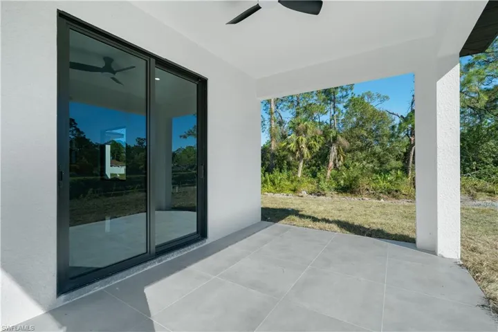 Covered patio featuring large format tile flooring, a ceiling fan, and sliding glass doors, with a natural landscape backdrop