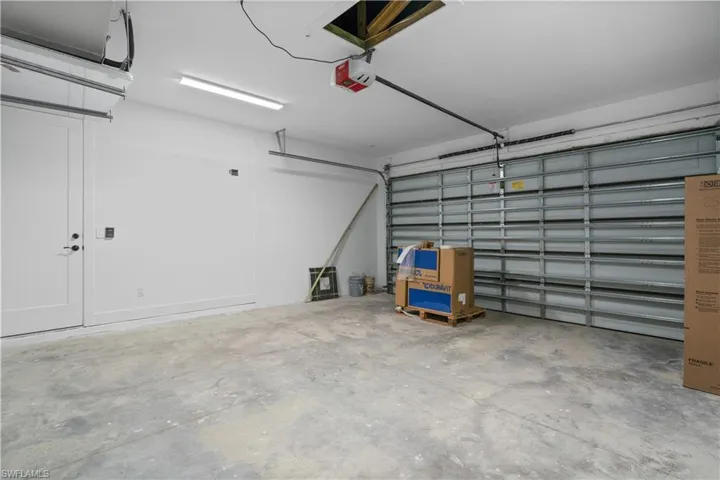 Spacious garage featuring a concrete floor, bright overhead lighting, and a white interior door with black hardware