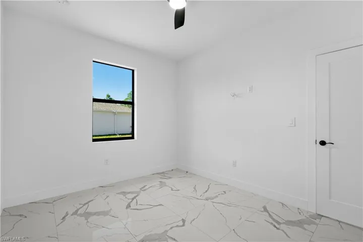Bright room with white walls, featuring a single window with black trim, a black ceiling fan, white baseboards, and marble-look tile flooring