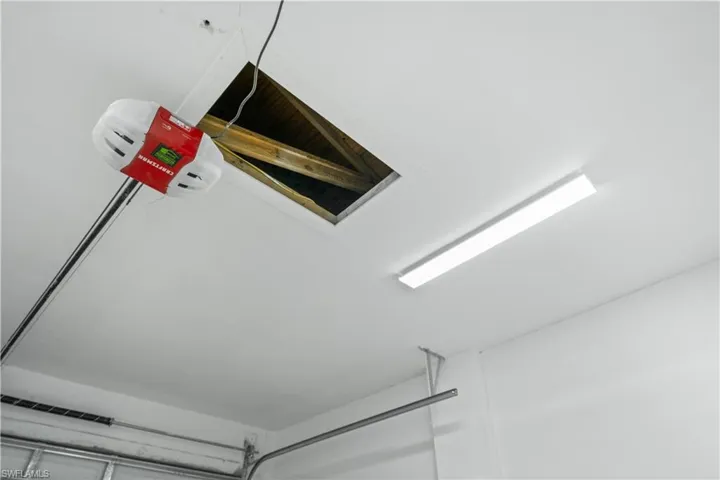 Garage ceiling featuring a white painted finish, flush-mount fluorescent lighting, and an attic access opening