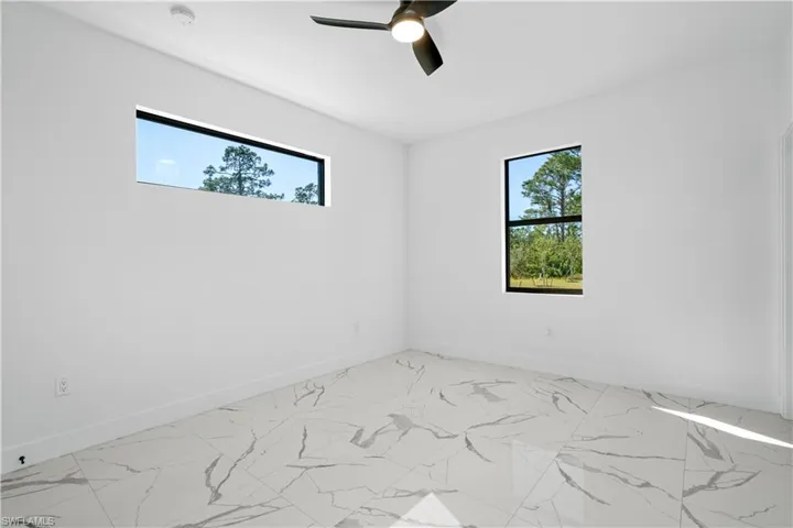 Spacious interior room featuring large format tile flooring with a marble-effect pattern, a contemporary ceiling fan, and two distinct window styles