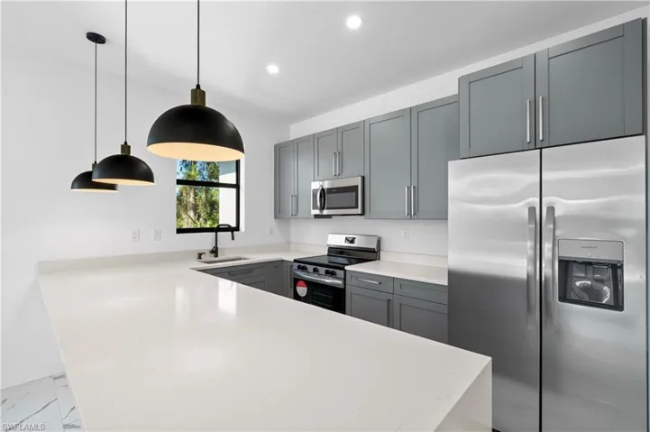Modern kitchen featuring light countertops, gray cabinetry, stainless steel appliances, and a window above the sink