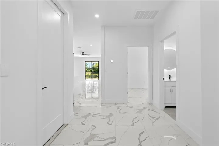 Contemporary interior featuring large format marble-look tile flooring, bright white walls, recessed lighting, and a modern bathroom vanity with an illuminated round mirror
