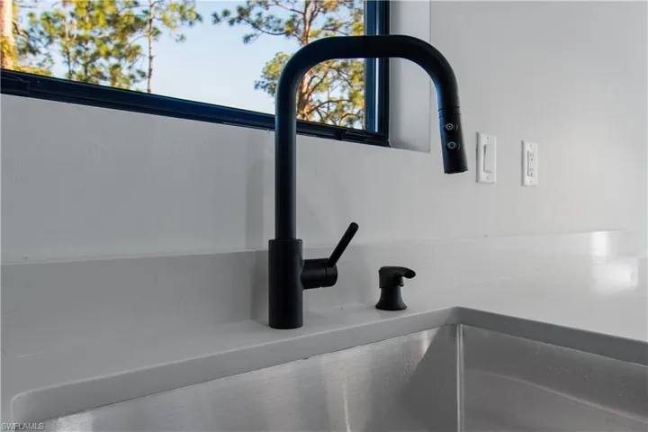 Kitchen sink featuring a matte black gooseneck faucet with an integrated sprayer, undermount stainless steel sink, and light-toned solid surface countertops