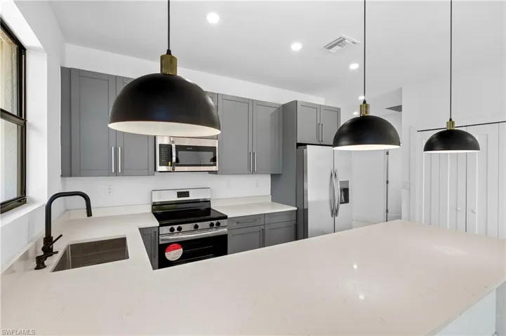 Modern kitchen featuring light-toned countertops, gray cabinetry, and three pendant lights over a central island