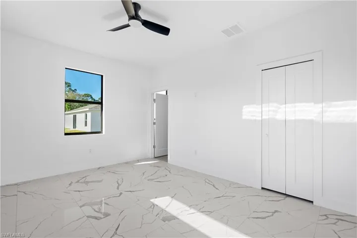 Bright room featuring white walls, large format tile flooring with a marbled pattern, a black ceiling fan, and a bi-fold closet door