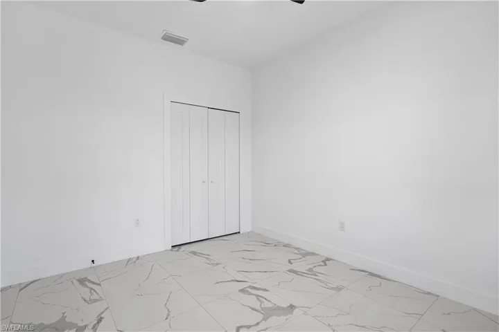 Bright interior space featuring large format tile flooring with distinctive veining, white walls, and a bi-fold closet door