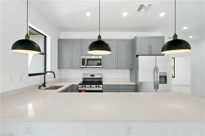 Modern kitchen featuring light gray cabinetry, stainless steel appliances, a black faucet, and white countertops