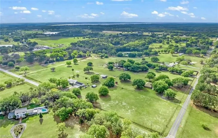 Expansive green landscape featuring scattered trees, residential structures, and a paved road