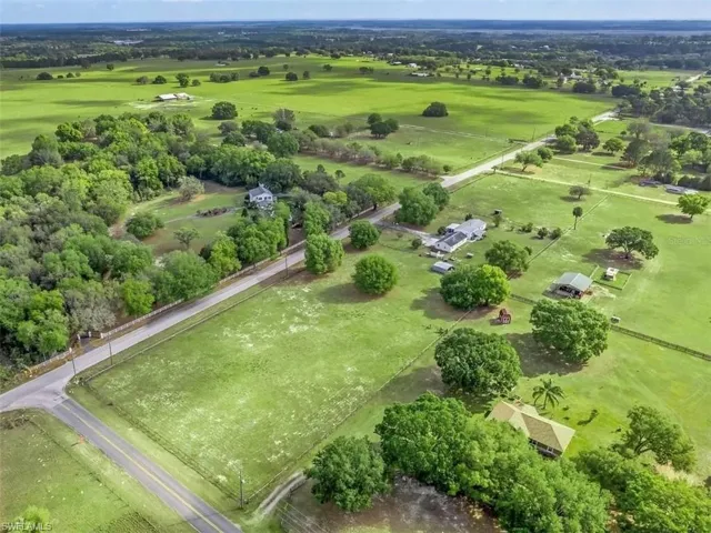 Expansive green acreage featuring multiple residential structures, mature trees, and paved road access