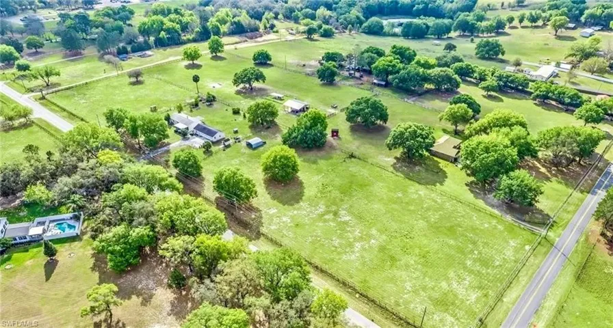 Expansive green acreage featuring scattered mature trees, a private road, and a paved public road bordering the property