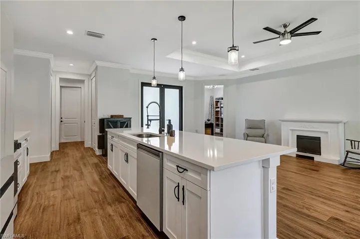 Kitchen featuring a kitchen island with sink, sink, stainless steel dishwasher, ornamental molding, and wood-type flooring