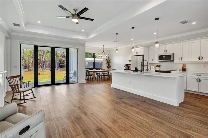 Kitchen with hardwood / wood-style flooring, pendant lighting, white cabinets, and an island with sink