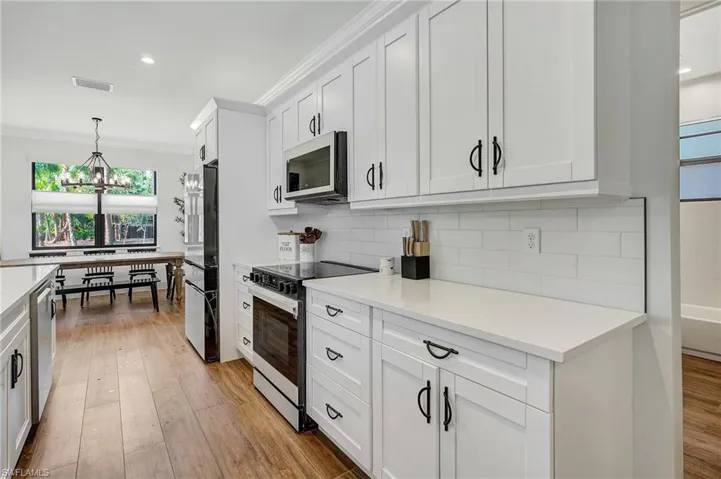Kitchen with white cabinetry, ornamental molding, stainless steel appliances, and light hardwood / wood-style floors