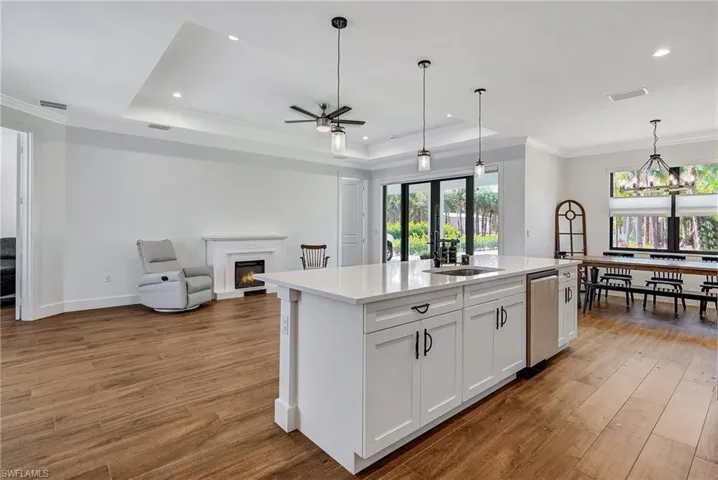 Kitchen with white cabinetry, light hardwood / wood-style flooring, an island with sink, pendant lighting, and ceiling fan with notable chandelier