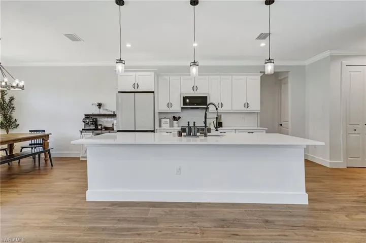 Kitchen featuring decorative light fixtures, white fridge, white cabinetry, and an island with sink