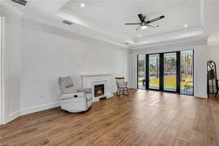 Living area with light wood-type flooring, a tray ceiling, ceiling fan, and ornamental molding