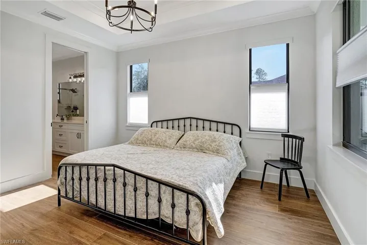 Bedroom featuring ensuite bathroom, crown molding, a chandelier, and hardwood / wood-style flooring