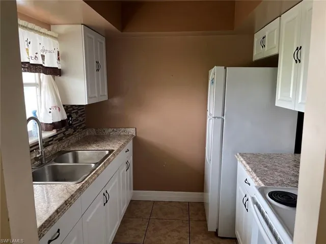 Kitchen featuring tile patterned floors, decorative backsplash, white cabinets, sink, and stove