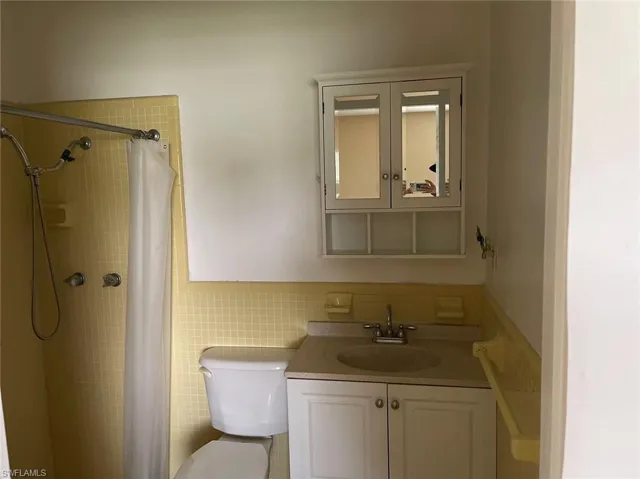 Bathroom featuring tile walls, toilet, vanity, and a shower with shower curtain
