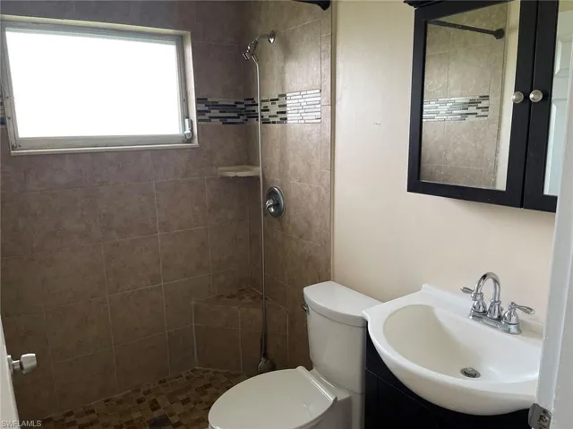Bathroom featuring toilet, vanity, and a tile shower
