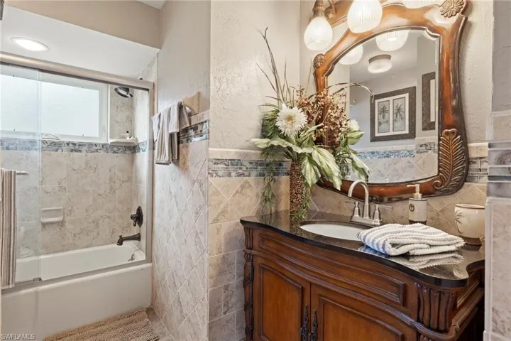 Bathroom featuring combined bath / shower with glass door, vanity, and tile walls