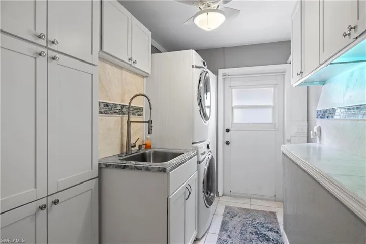 Laundry area with cabinets, sink, ceiling fan, light tile patterned floors, and stacked washer / drying machine