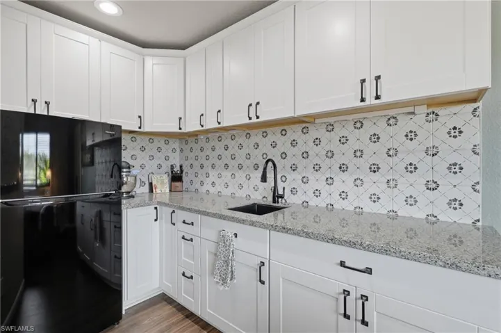 Kitchen featuring white shaker cabinetry with matte black hardware, light-colored granite countertops, and a patterned tile backsplash