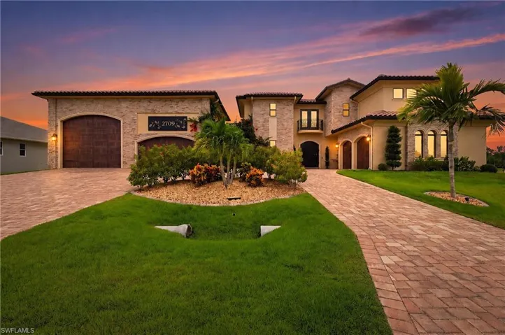 Stately exterior featuring a paver driveway, stone accents, arched garage doors, and mature landscaping