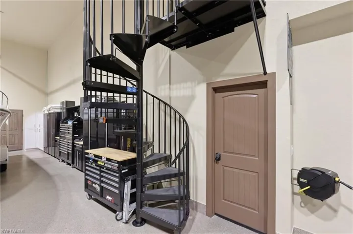 Black metal spiral staircase providing access to an upper level, with light beige walls and a neutral-toned floor