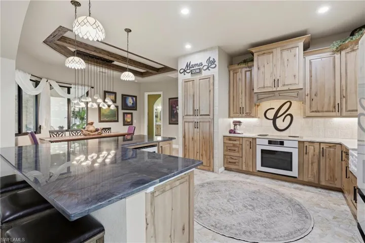 Spacious kitchen featuring an expansive island with a polished countertop, light wood cabinetry, built-in oven, tile backsplash, and recessed lighting