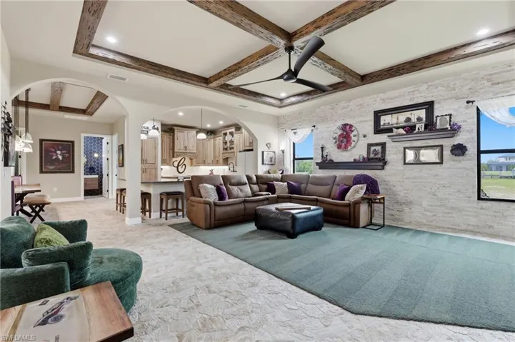 Living area with coffered wood-beam ceiling, white brick accent wall, and multiple windows